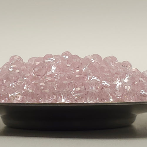 Pink faceted glass beads piled in a shallow black dish against a plain light gray background.