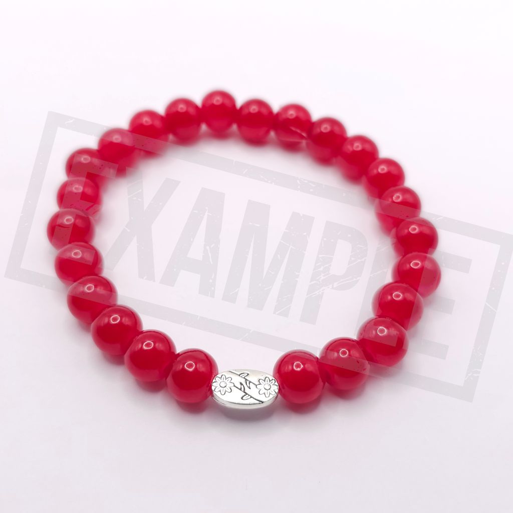 An agate red beaded bracelet with a small silver oval charm featuring a floral pattern displayed on a white background.