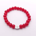 A red beaded bracelet with a small silver oval charm featuring a floral pattern, photographed on a clean white background.