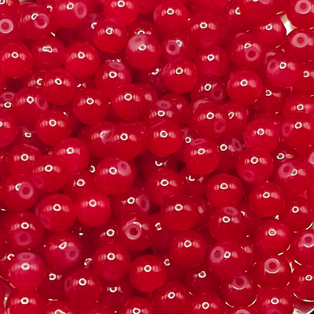 A close-up pile of small, glossy red translucent beads with a central hole, filling the entire frame.