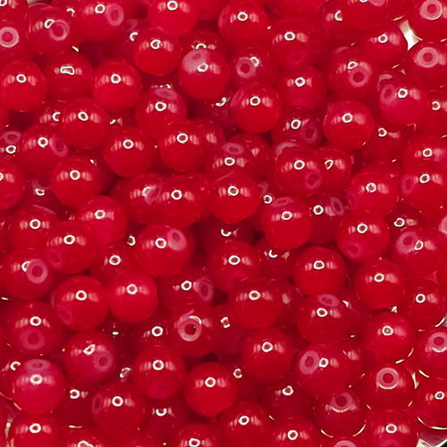 A close-up pile of small, glossy red translucent beads with a central hole, filling the entire frame.