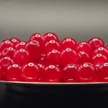 A pile of glossy, translucent red glass beads resting on a dark surface against a dark gray background.