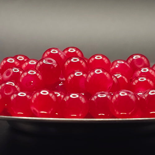 A pile of glossy, translucent red glass beads resting on a dark surface against a dark gray background.