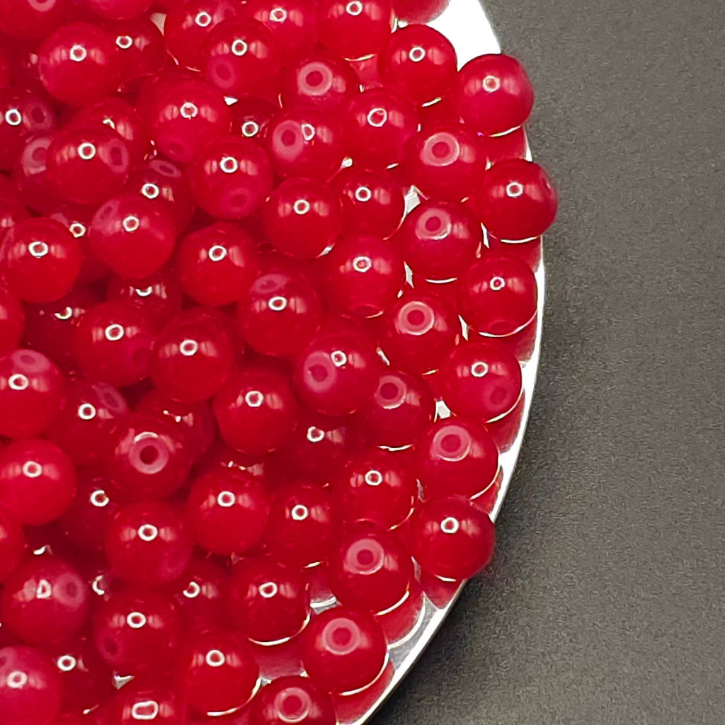 Red translucent round beads with center holes, piled on a silver tray against a dark gray background.