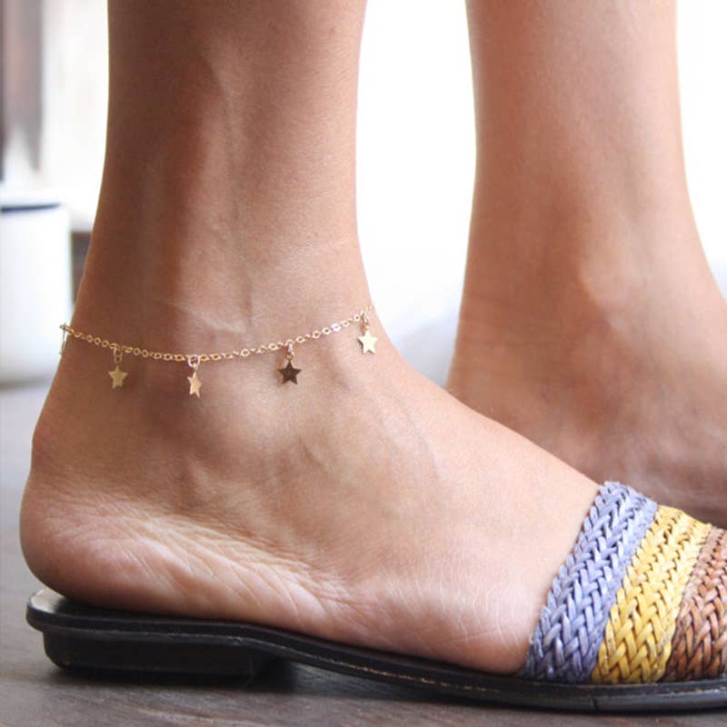 Ankle with gold star anklets and colourful woven anklets on a neutral background