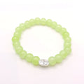 A beaded stretch bracelet made of light green translucent round beads, featuring a silver oval charm with a small clear floral design, shown on a plain white background.