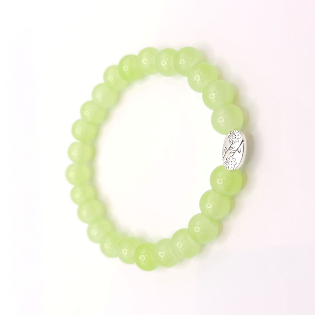 A beaded stretch bracelet made of light green translucent round beads, featuring a silver oval charm with a small clear floral design, shown on a plain white background.