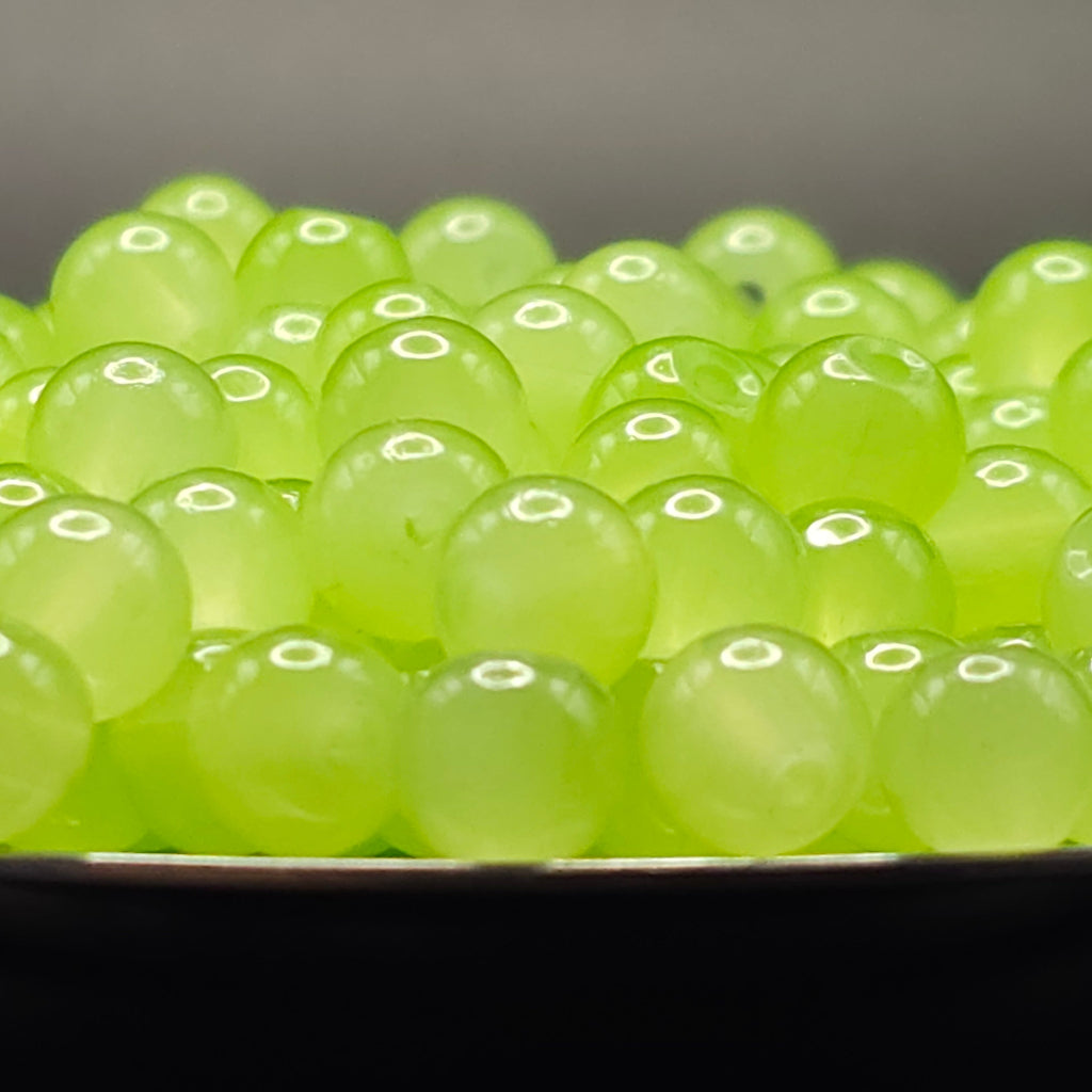 A close-up of many translucent light green gel beads or boba pearls piled in a bowl, with a dark background.