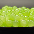 A close-up of many translucent light green gel beads or boba pearls piled in a bowl, with a dark background.