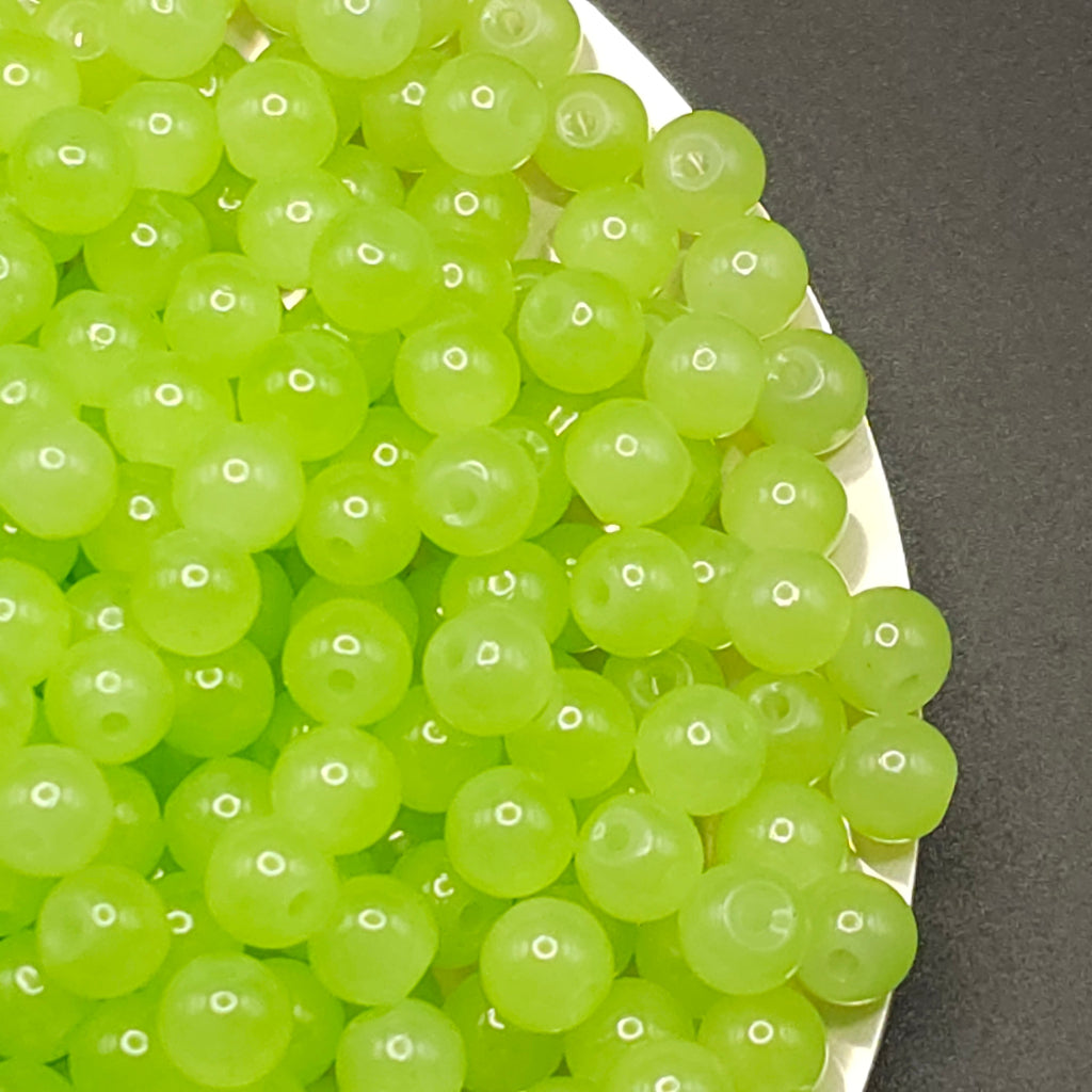 A pile of translucent light green round beads with hollow centers, shown close-up on a white plate against a dark gray background.