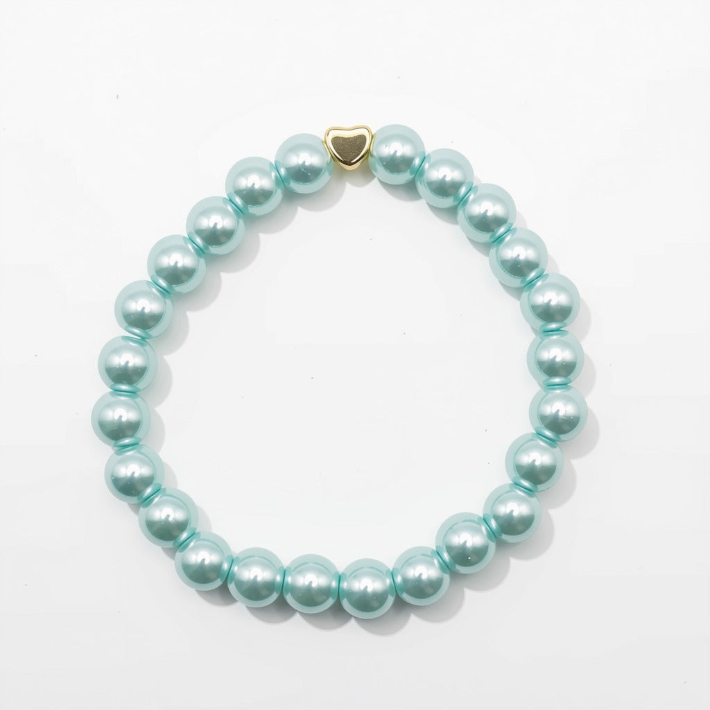 A beaded stretch bracelet made of glossy, light aquamarine pearlised glass beads with a small gold heart-shaped charm, displayed on a clean white background.