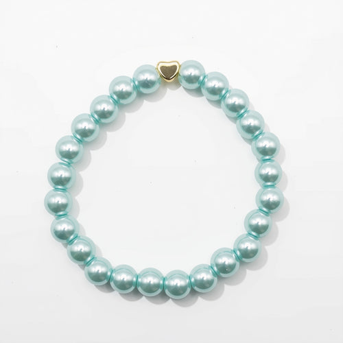 A beaded stretch bracelet made of glossy, light aquamarine pearlised glass beads with a small gold heart-shaped charm, displayed on a clean white background.
