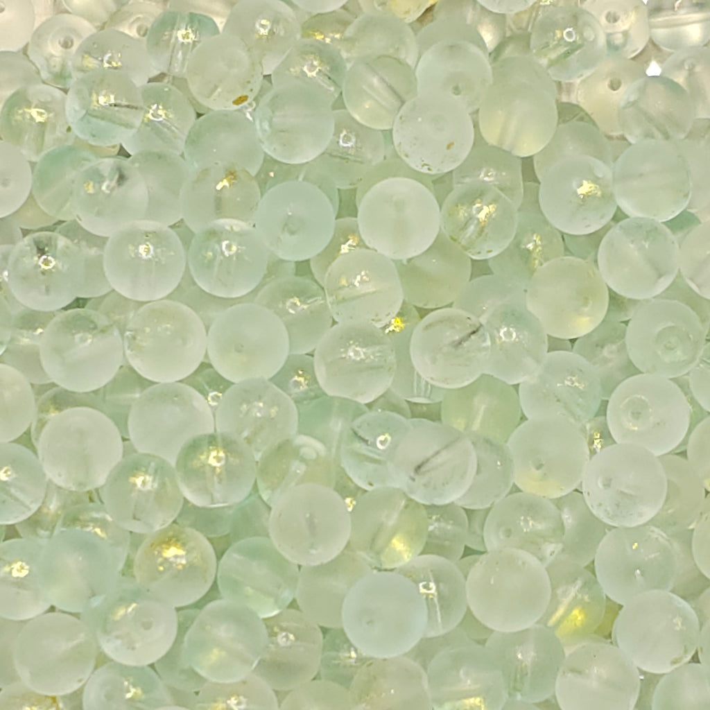 A close-up pile of small round translucent beads in a pale mint green color with subtle gold glitter flecks inside.