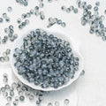Gray translucent glass beads scattered on a white textured surface, with a white shell-shaped dish filled with the beads in the center.