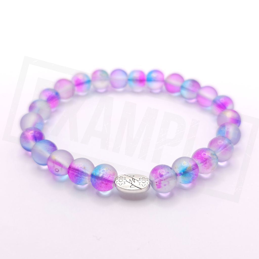 A beaded stretch bracelet featuring translucent purple, pink, and blue iridescent beads with a small silver-toned oval charm engraved with a floral motif, displayed on a white background.