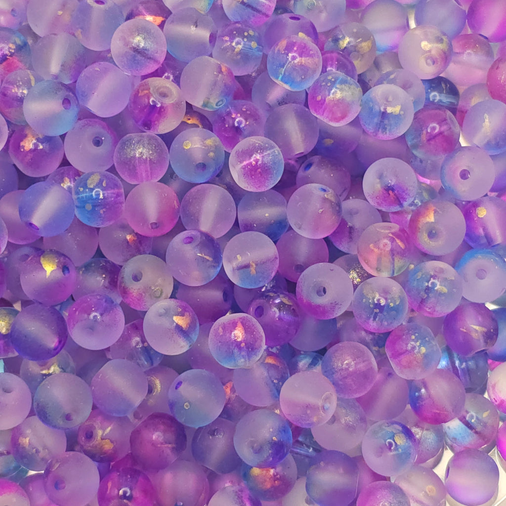 A close-up pile of round acrylic beads with a frosted lavender and purple finish, featuring iridescent glitter flecks that catch the light.
