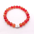 A beaded stretch bracelet made of round translucent orange-red beads with a small silver oval charm featuring a floral design.