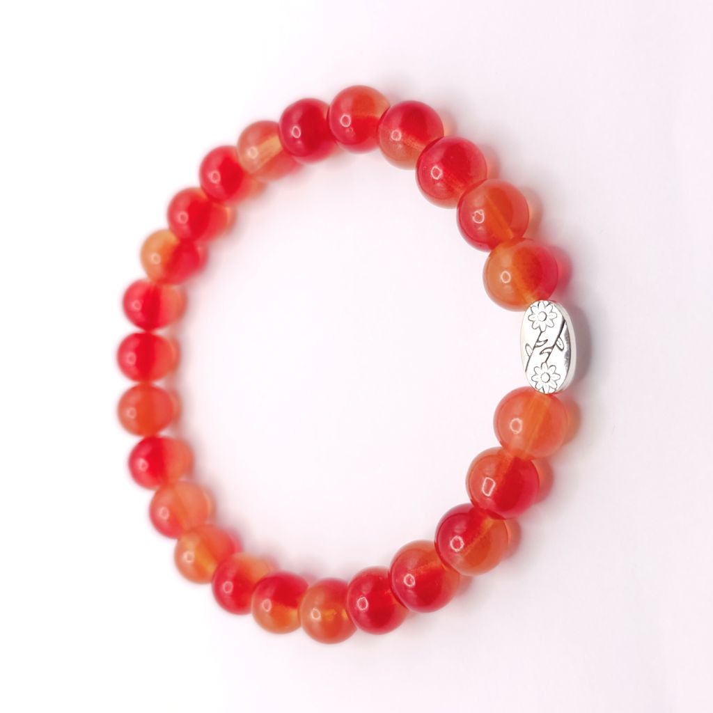 A beaded stretch bracelet made of round translucent orange-red beads with a small silver oval charm featuring a floral design.