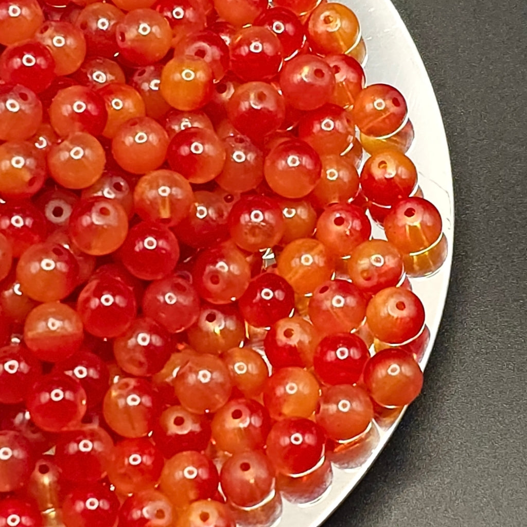 Close-up of many round translucent red and orange beads with holes, piled on a white plate against a dark gray surface.
