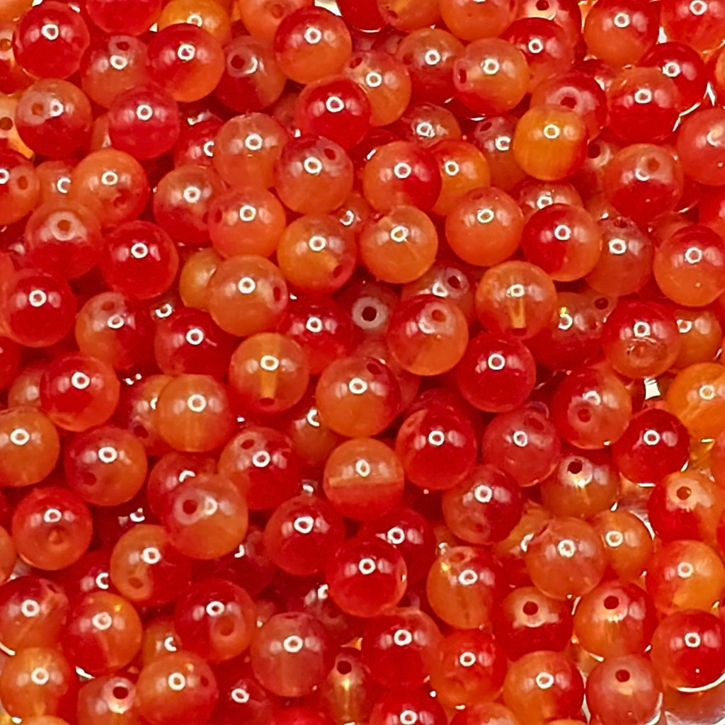 A close-up pile of small round translucent beads in shades of red, orange, and pink with glossy highlights.
