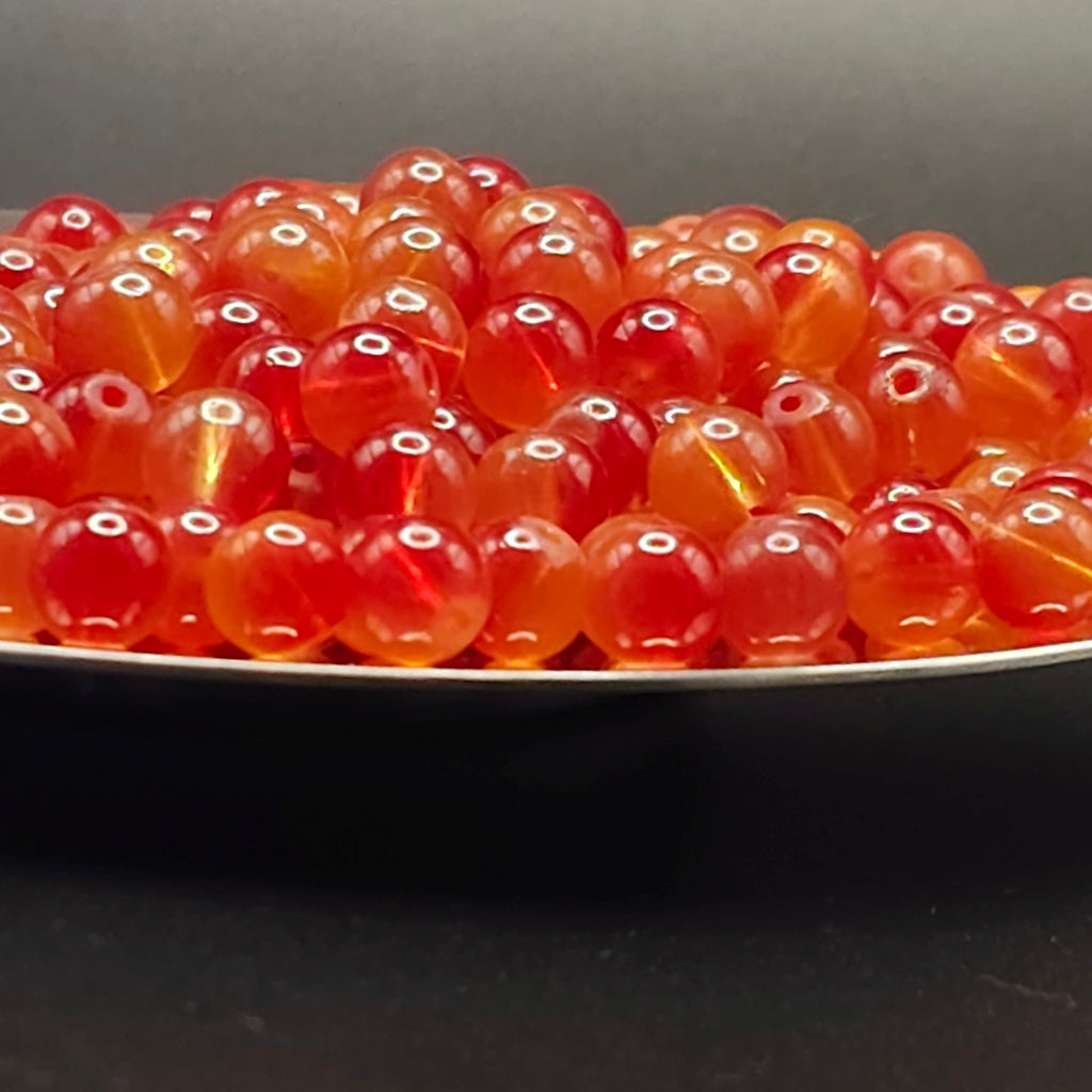 A close-up of many small translucent red-orange beads piled in a shallow dish against a dark background.