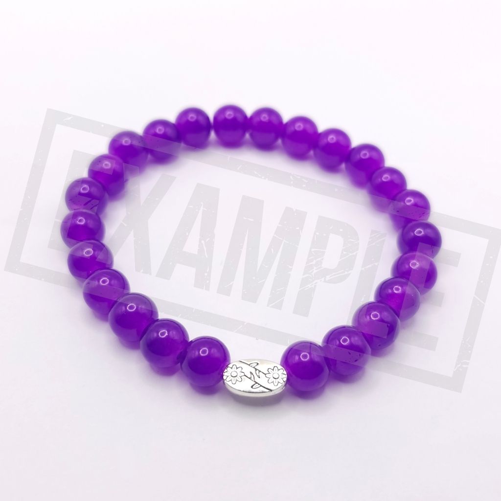 A crystal purple beaded bracelet with a silver oval charm featuring a floral design, displayed on a white background.