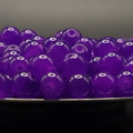 A pile of translucent purple glass beads with a central hole, resting on a dark surface against a dark gray background.