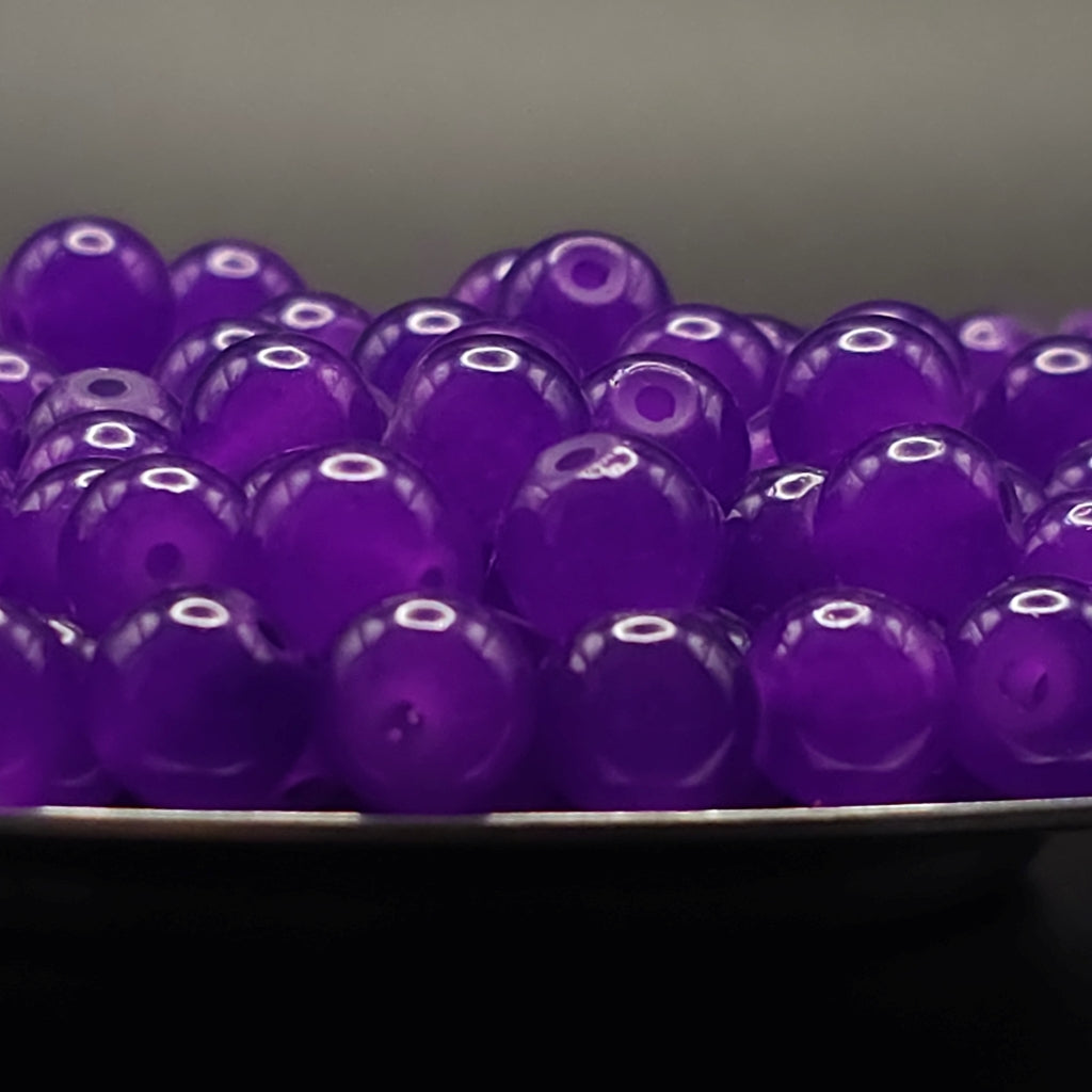 A pile of translucent purple glass beads with a central hole, resting on a dark surface against a dark gray background.