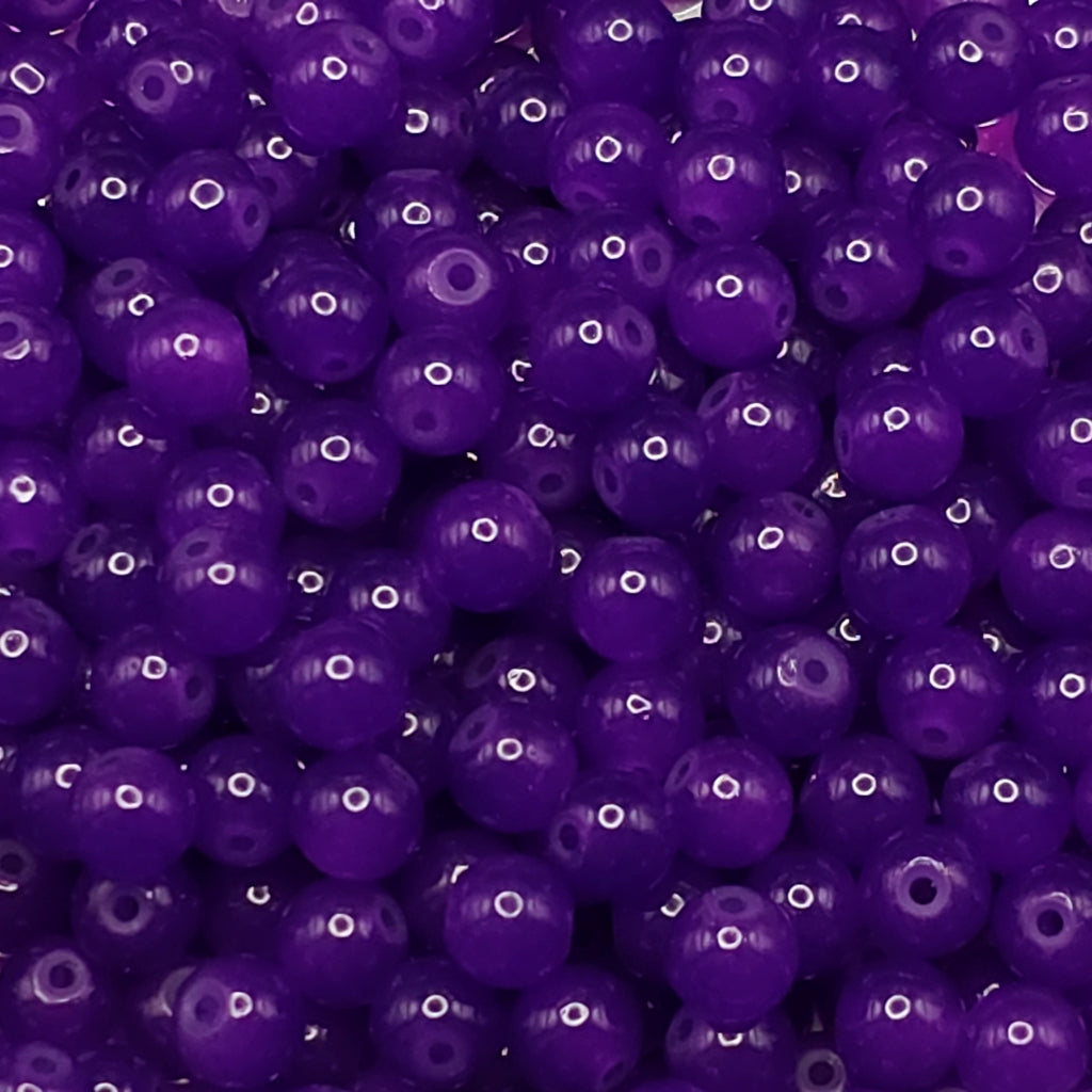 A close-up pile of glossy, round purple beads with central holes, filling the entire frame.