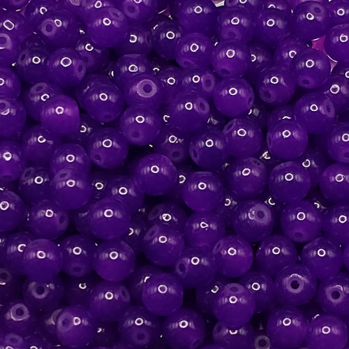 A close-up pile of glossy, round purple beads with central holes, filling the entire frame.