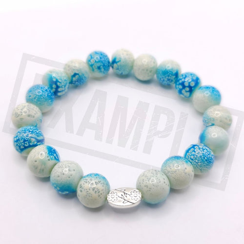 A beaded stretch bracelet featuring light blue and white marbled glass beads, with a small silver oval charm, on a white background.