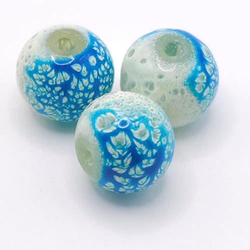 Three round glass beads with a blue and white floral pattern, displayed on a clean white background.