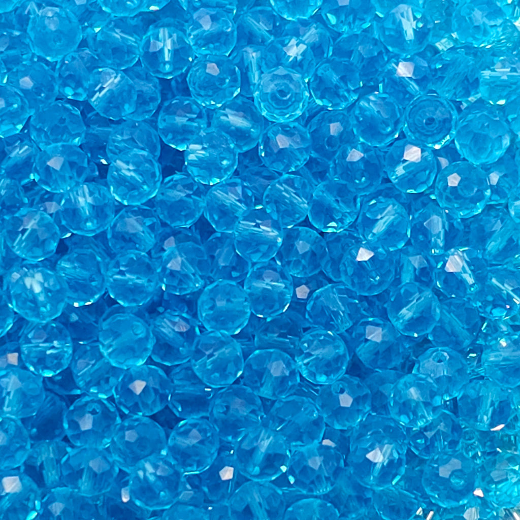 A close-up pile of faceted round blue beads, showing their transparent, crystal-like texture and shiny highlights.