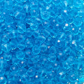 A close-up pile of faceted round blue beads, showing their transparent, crystal-like texture and shiny highlights.