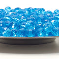 Blue faceted crystal beads piled in a shallow dish on a white background.