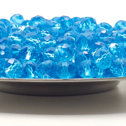 Blue faceted crystal beads piled in a shallow dish on a white background.