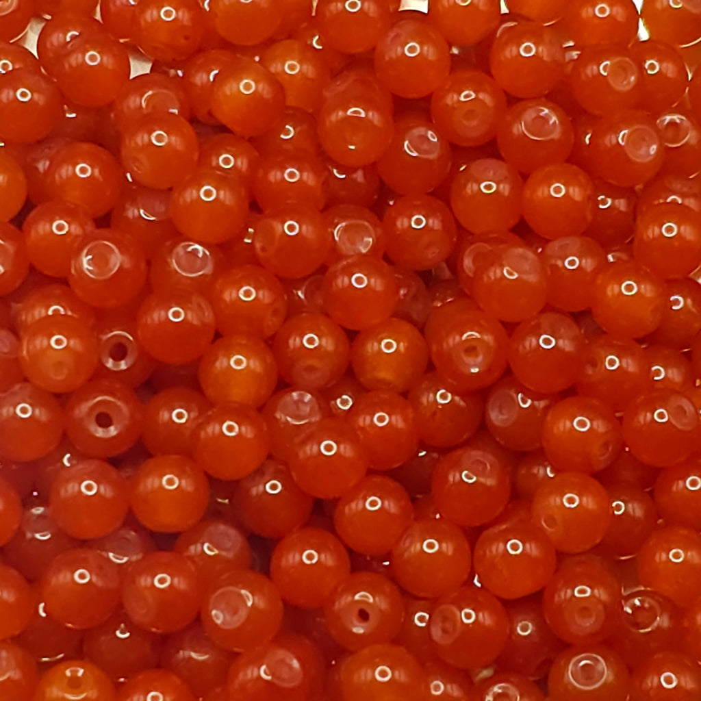 A close-up pile of small, round, translucent orange-red beads with a glossy finish and central holes.