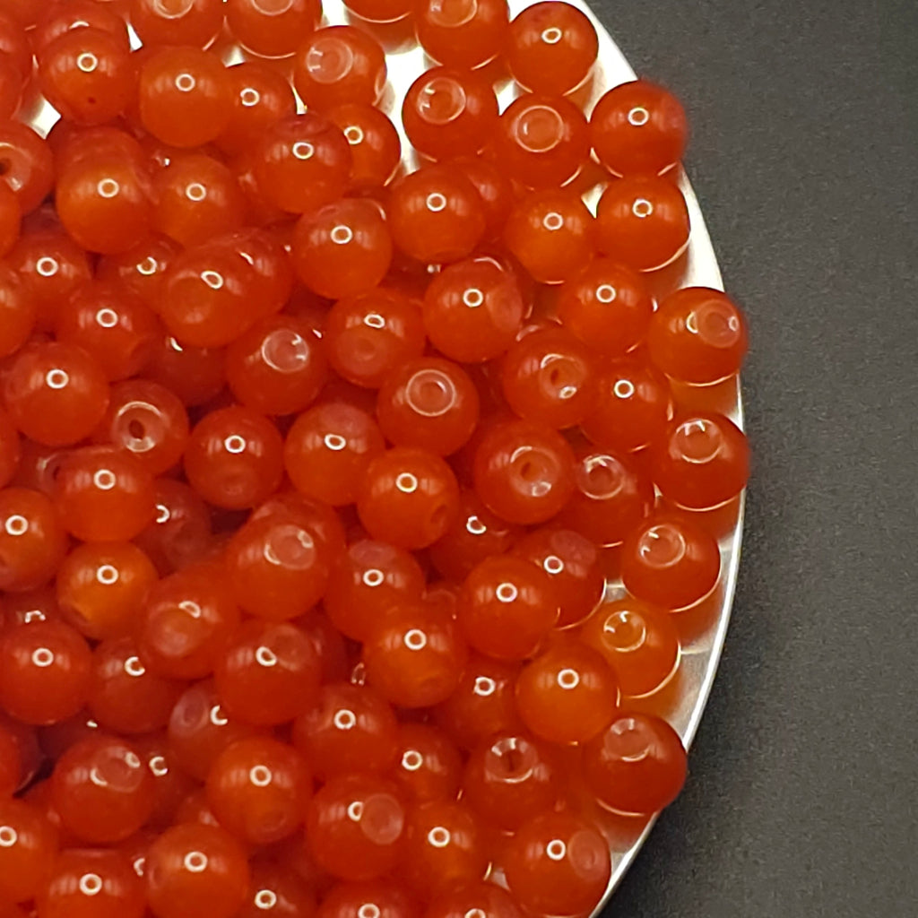 A close-up of many small translucent orange-red round beads or cabochons piled on a white plate against a dark gray background.