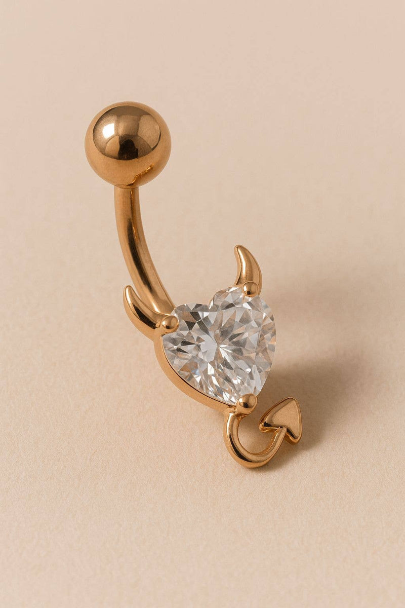 Gold belly button ring with a heart-shaped gem on a beige background