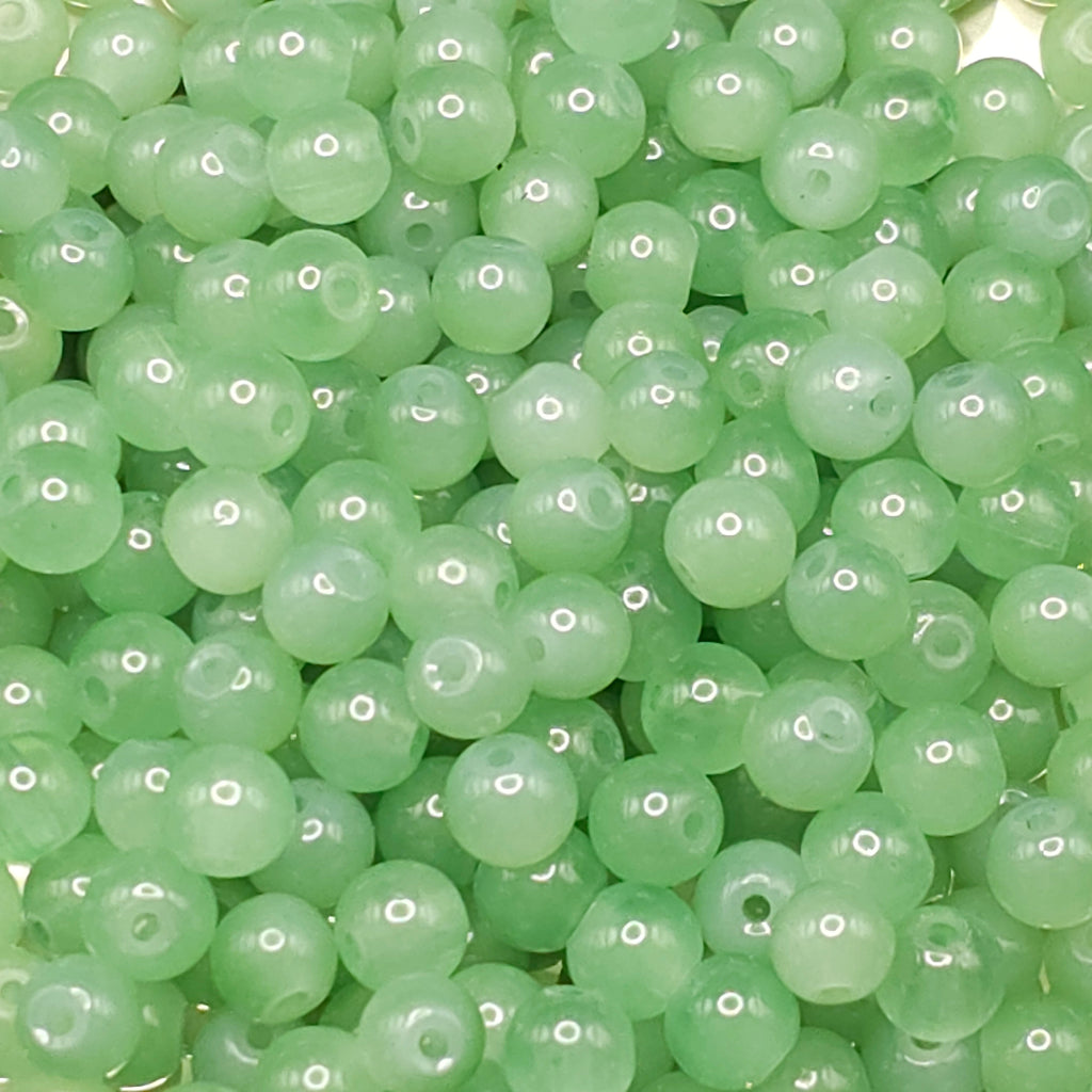 A close-up pile of round, light green translucent beads with drilled holes, filling the entire frame.