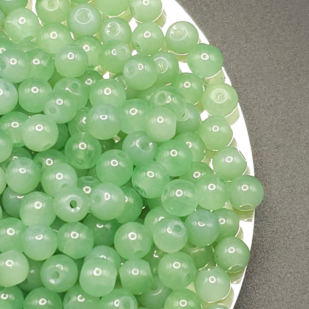 A pile of light green translucent round beads with drilled holes, resting on a white plate against a gray background.