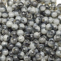 A close-up pile of round glass beads with a mottled black, white, and gray pattern, showing glossy highlights.