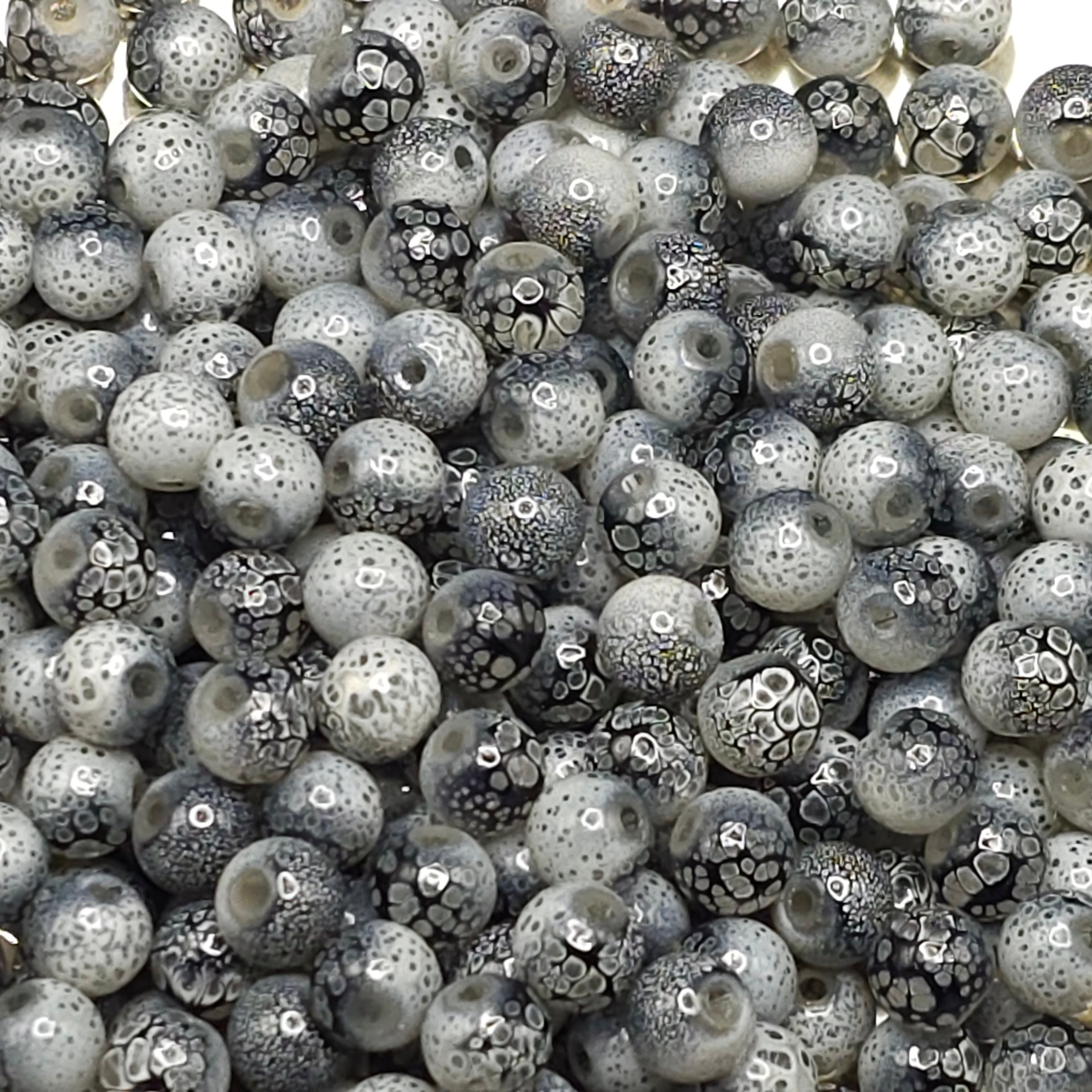 A close-up pile of round glass beads with a mottled black, white, and gray pattern, showing glossy highlights.