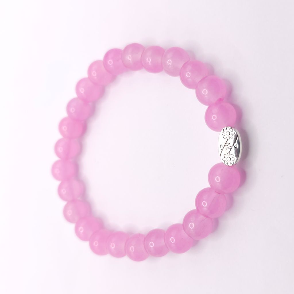 A pink beaded stretch bracelet with a small silver-toned oval charm featuring a floral pattern, displayed on a clean white background.