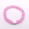 A pink beaded stretch bracelet with a small silver-toned oval charm featuring a floral pattern, displayed on a clean white background.