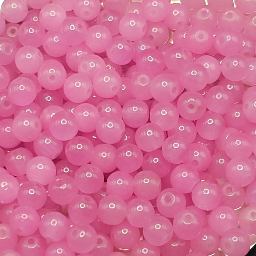 A close-up pile of small, round, translucent pink beads with a glossy finish and a central hole.