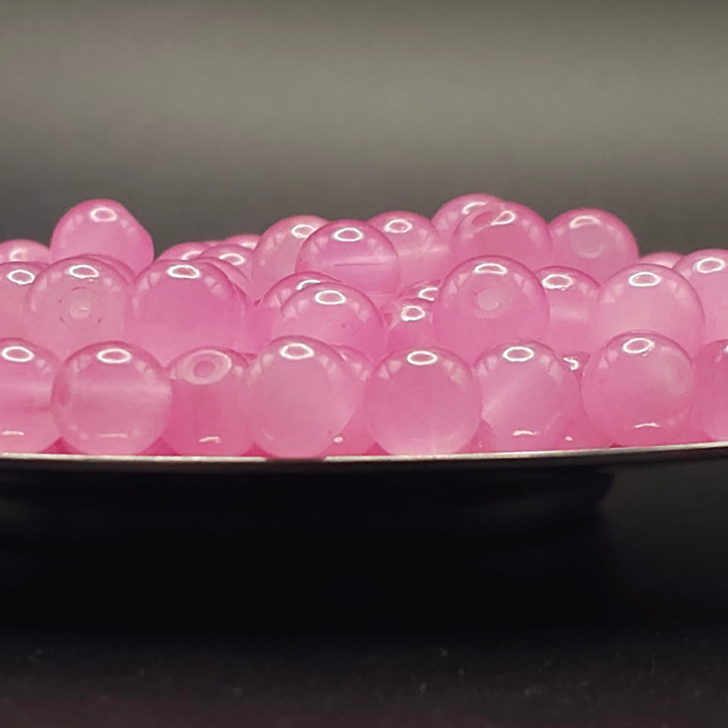 Pink translucent round beads or boba pearls piled on a dark surface against a dark gray background.