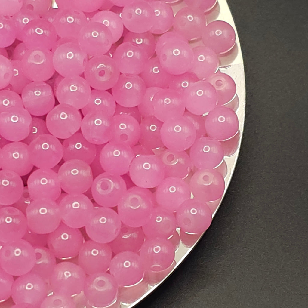 A close-up of many small translucent pink round beads with central holes, arranged on a silver tray against a dark gray background.