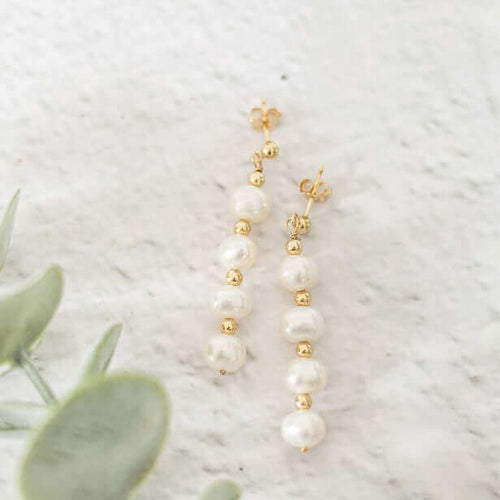 Pearl and gold drop earrings on a light background with greenery