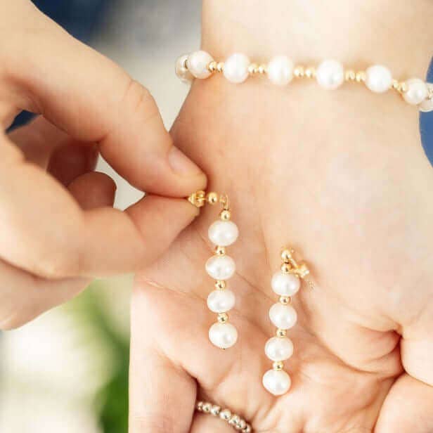 Pearl earrings being worn on a hand with a blurred background